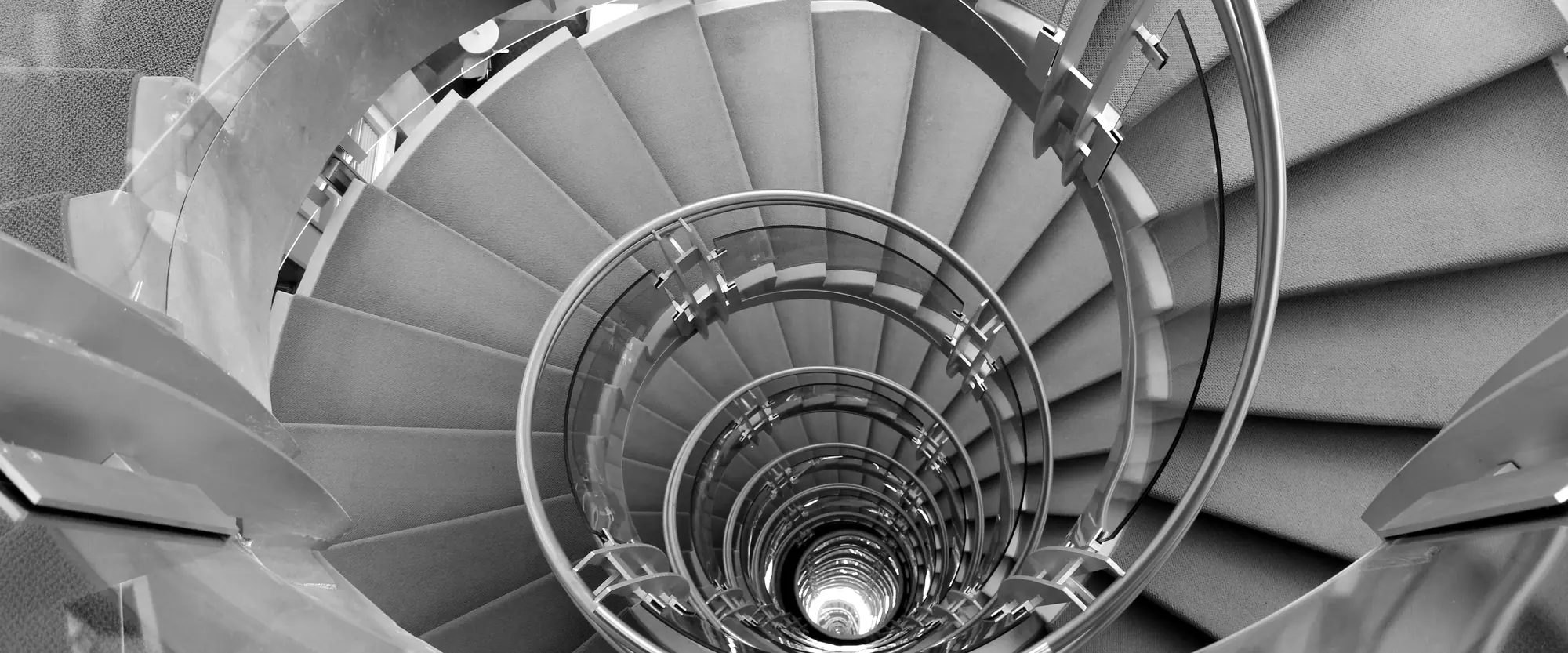 Un escalier en colimaçon photographié d’en haut, ses volées s’éloignant vers un point de lumière au centre.